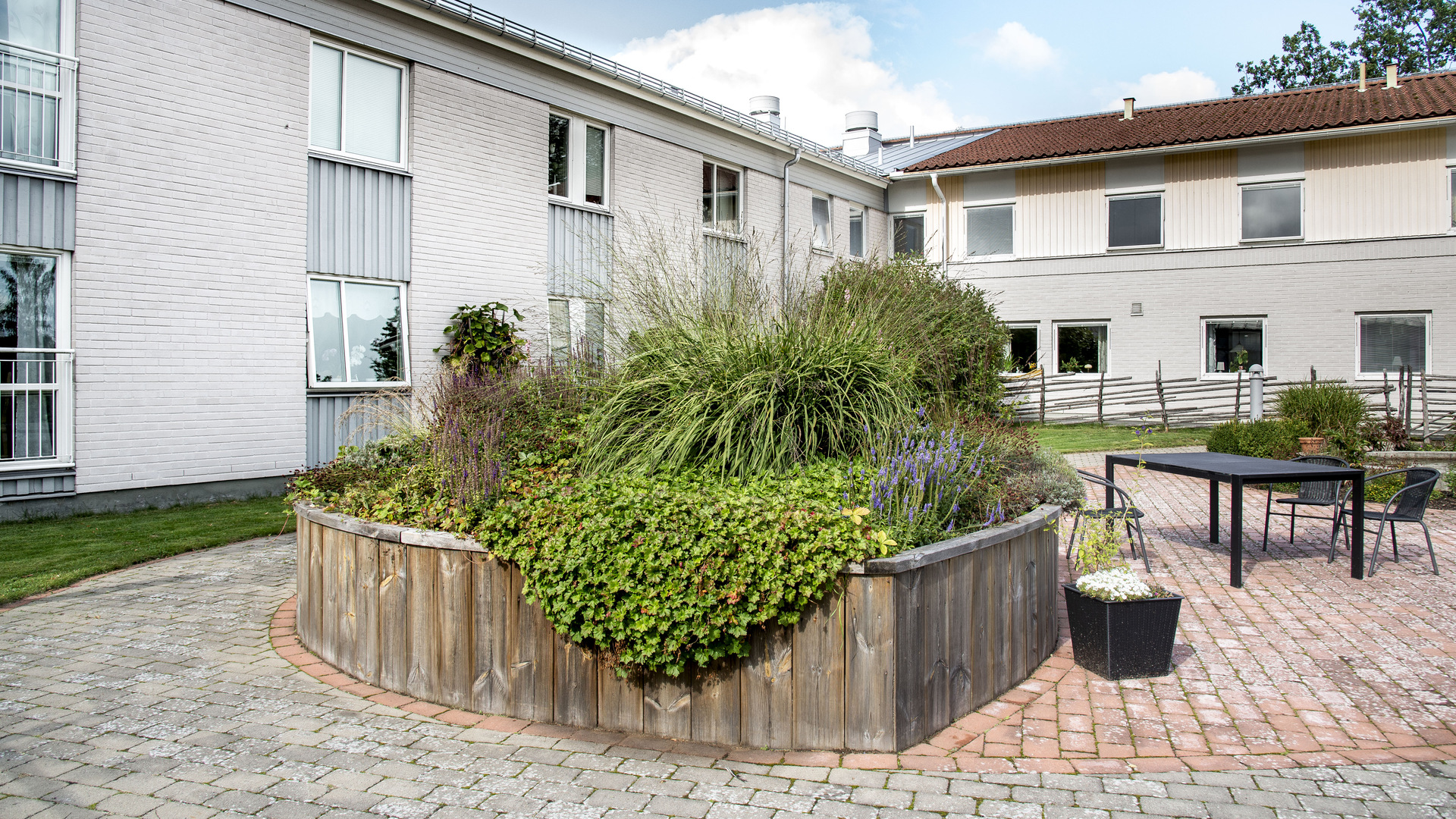 Innergård med utemöbler och blomsterrabatter och stenlagd uteplats. 